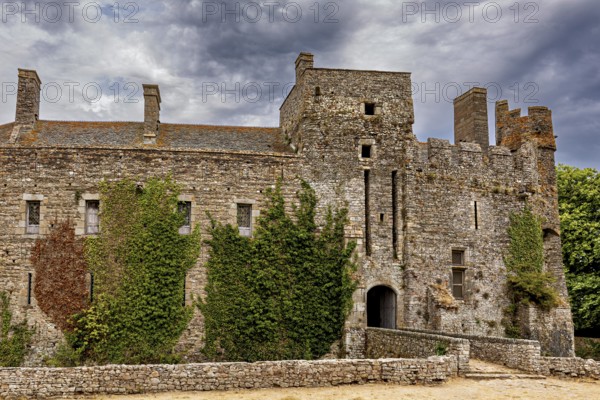 Detailed view of a castle with battlements and ivy under a cloudy sky, Pirou Castle in Normandy, France