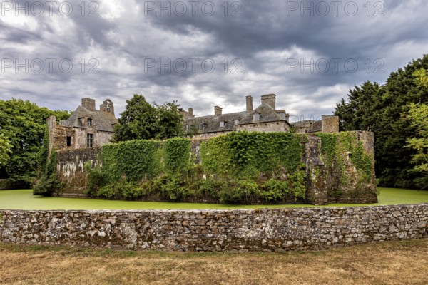 Wide-angle shot of a castle with ivy-covered wall and cloudy sky, Pirou Castle in Normandy, France