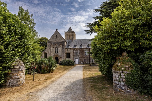 Historic church with a path surrounded by green trees and blooming nature, The Abbey de La Lucerne in Normandy, France