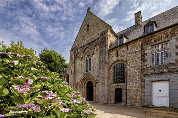 Historic stone church with colourful flowers in the foreground under a blue sky, The Abbey de La Lucerne in Normandy, France