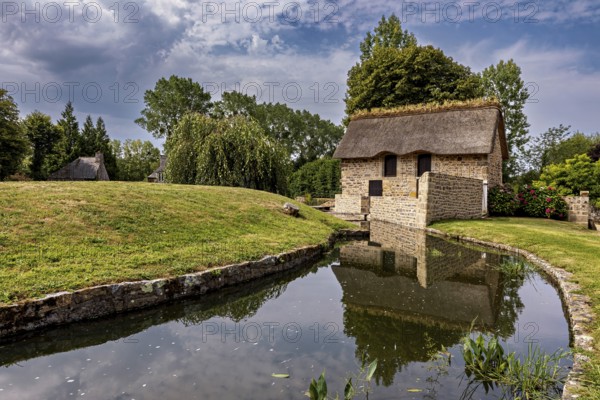 Small house with thatched roof in a quiet, green setting by a stream, The Abbey of La Lucerne in Normandy, France