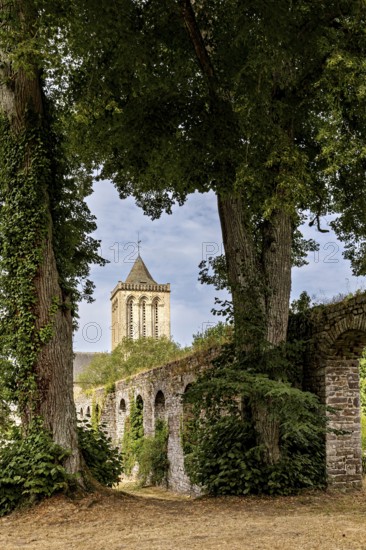 A tower surrounded by tall trees and an overgrown stone wall in a tranquil setting, The Abbey of La Lucerne in Normandy, France