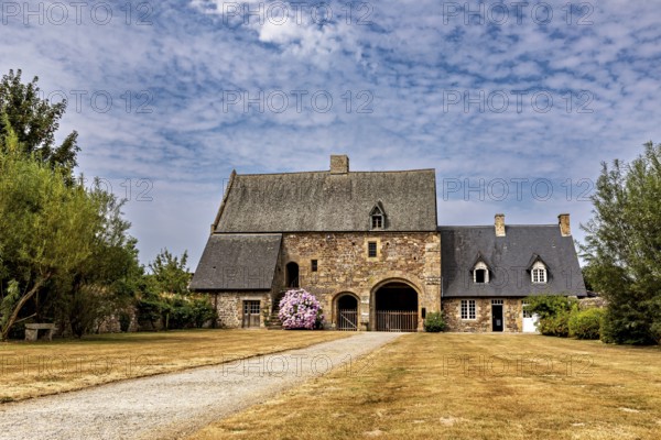 An old stone house with a gravelled path and a blue sky, surrounded by manicured lawns, The Abbey of La Lucerne in Normandy, France