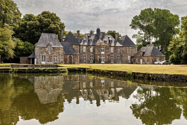 A historic castle behind a tranquil pond with a reflection and trees, The Abbey de La Lucerne in Normandy, France