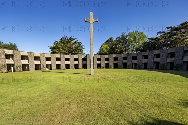A stone cross sits enthroned in the centre of a green, circular courtyard surrounded by a concrete structure, German soldiers' cemetery from the Second World War near Huisnes-sur-Mer in Normandy, France