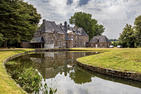 A castle with a moat in a green setting, surrounded by trees and clouds in the sky, The Abbey of La Lucerne in Normandy, France