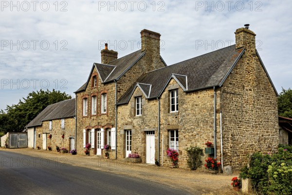 Historic stone houses along a village street with flowering windows, Historic houses in Normandy in France