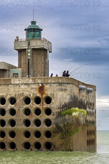 Concrete building with lighthouse and anglers at the water's edge, under a cloudy sky, The harbour pier of Dieppe in Normandy, France