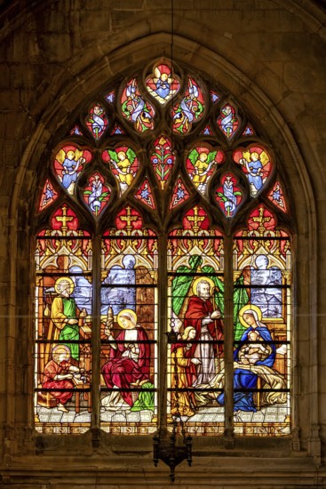 A Gothic stained glass window shows a religious scene with the Holy Family and angels in bright colours, The stained glass windows of Dieppe Cathedral in Normandy, France