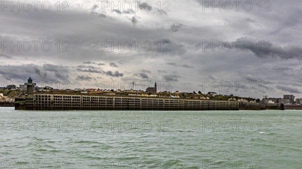 Massive harbour wall under a cloudy sky, surrounded by the sea in a stormy atmosphere, The harbour pier of Dieppe in Normandy, France