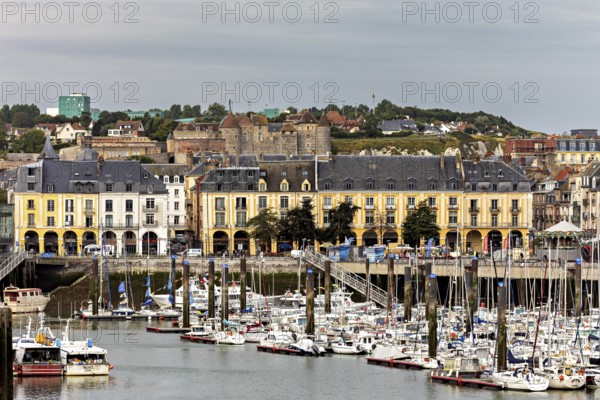 Yellow historic buildings overlook a busy harbour with many boats, The harbour of Dieppe in Normandy, France