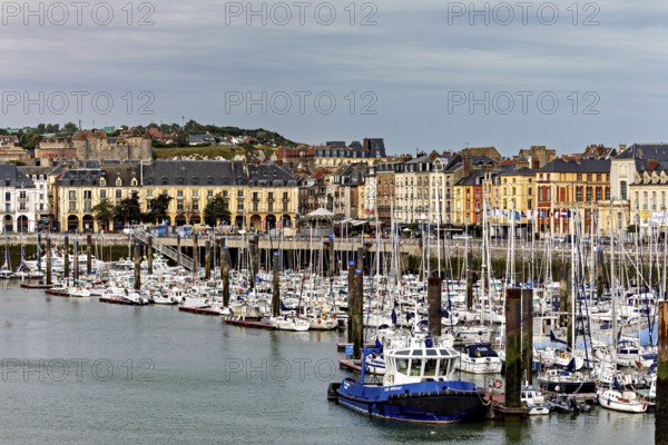 Cityscape with harbour and boats in front of a hilly backdrop under a cloudy sky, The harbour of Dieppe in Normandy, France