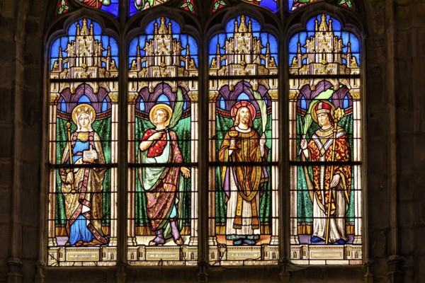 A Gothic church window shows colourful depictions of angels and saints in detailed stained glass, The church windows of Dieppe Cathedral in Normandy, France