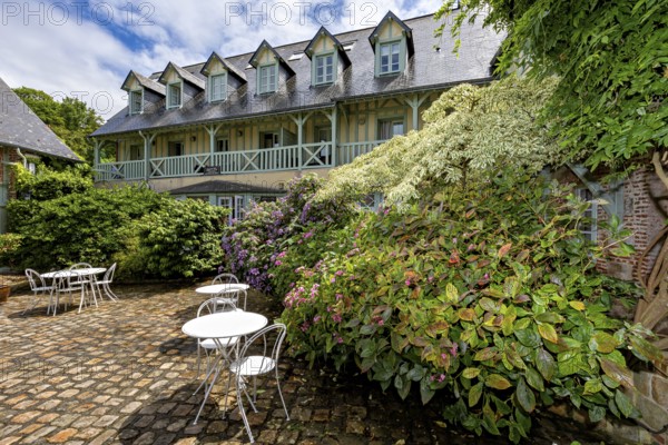 Lively garden with flowers and seating areas, surrounded by a backdrop of half-timbered houses, the historic mill village of Veules Les Roses in Normandy, France