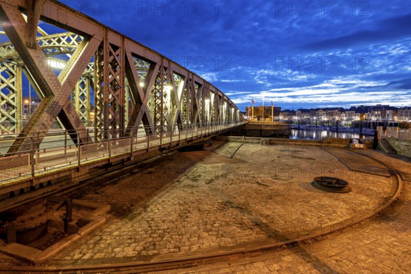 Metal bridge in evening city with illuminated sky and cloudy horizon, The swing bridge of Dieppe in Normandy, France
