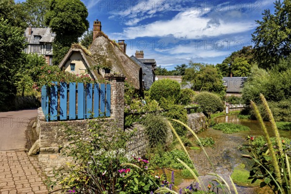 Thatched roof house with blue fence on a path surrounded by natural, picturesque landscape, The historic mill village of Veules Les Roses in Normandy, France