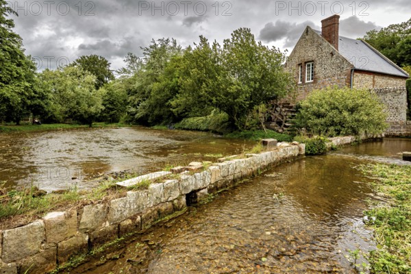 House by a river with a restored stone wall, surrounded by dense greenery, The historic mill village of Veules Les Roses in Normandy, France
