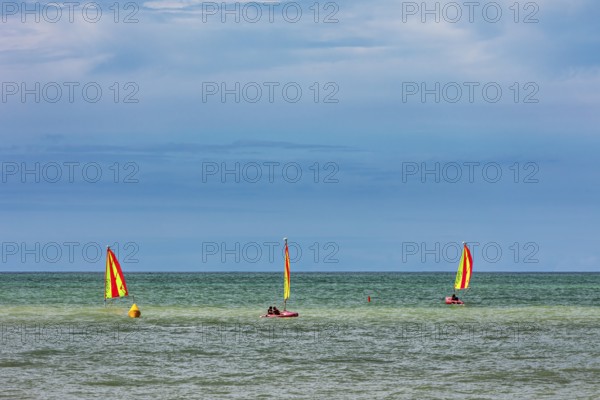 Three boats with yellow sails on the sea under a cloudy sky, surfers on the sea in Normandy, France