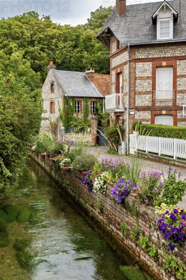 Beautifully landscaped canal with brick houses and flowers, surrounded by natural greenery, The historic mill village of Veules Les Roses in Normandy, France