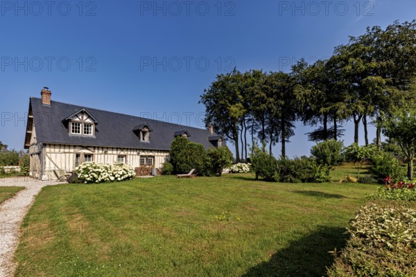 Inviting half-timbered house on a sunny day with a well-tended garden and stately trees, Historic houses in Normandy, France