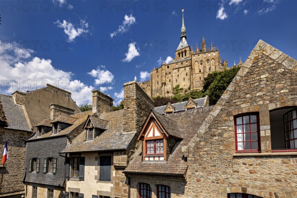 Stone and tiled roofs of ancient buildings with a dominant tower in the background under a clear sky, Mont Saint Michel in Normandy, France
