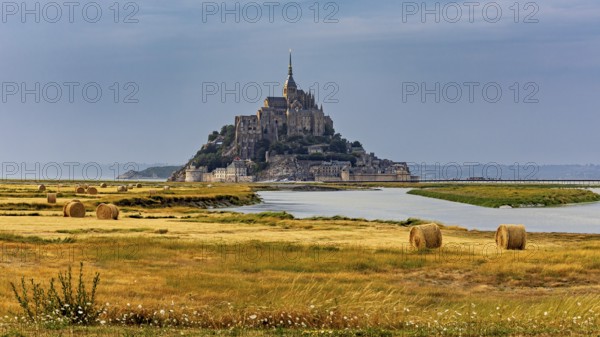 A castle rises in the middle of fields and a river, surrounded by bales of straw, Mont Saint Michel in Normandy, France