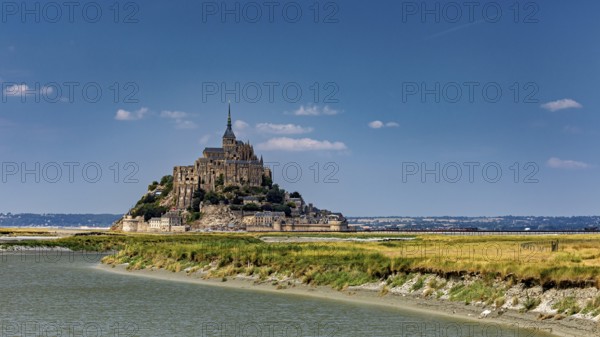 A majestic castle perched on the riverbank under a sunny sky, Mont Saint Michel in Normandy, France