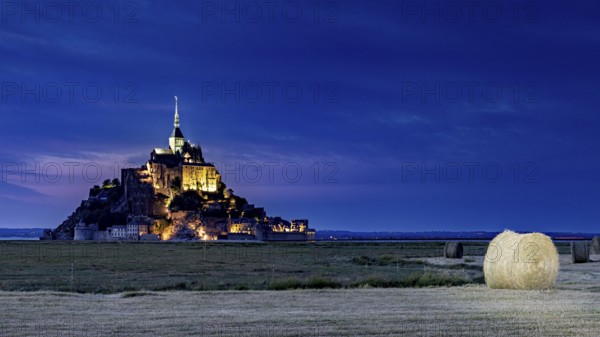 Mont Saint-Michel at night with a bale of hay in a field in the foreground, Mont Saint Michel in Normandy, France