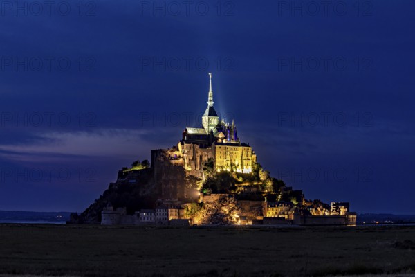 Historic monastery illuminated at night against a dark blue sky, Mont Saint Michel in Normandy, France