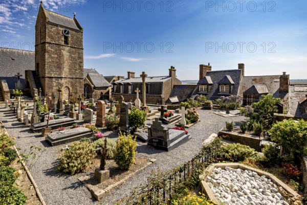 A peaceful cemetery next to a church with gravestones and flowers under a clear blue sky, The cemetery of Mont Saint Michel in Normandy, France