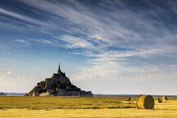 Mont Saint-Michel with dramatic sky and bales of straw in a wide field, Mont Saint Michel in Normandy, France