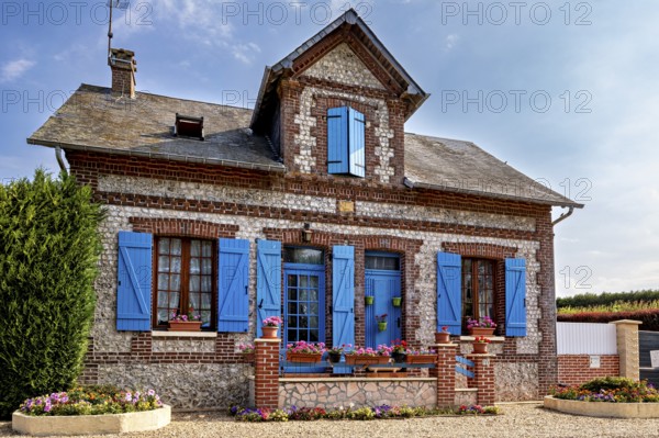 Historic stone house with blue shutters and blooming flowers in decorative plant beds, Historic houses in Normandy, France