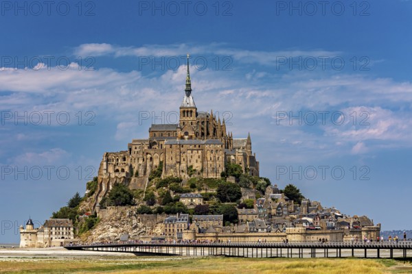 An imposing castle rises against a blue sky with a few clouds, Mont Saint Michel in Normandy, France