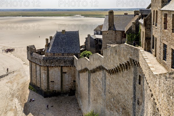 Historic castle wall with a view of a wide expanse of sand and distant buildings under a clear sky, Mont Saint Michel in Normandy, France