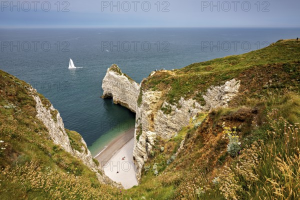 Green cliffs with sailing boat in the sea and small beach bay, The cliffs and alabaster coast of Etretat in Normandy France