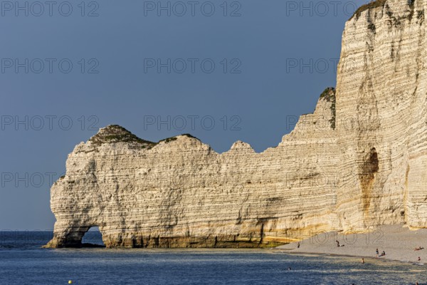 High cliffs form the coastline, overlooking a calm beach with clear skies, The cliffs and alabaster coast of Etretat in Normandy France