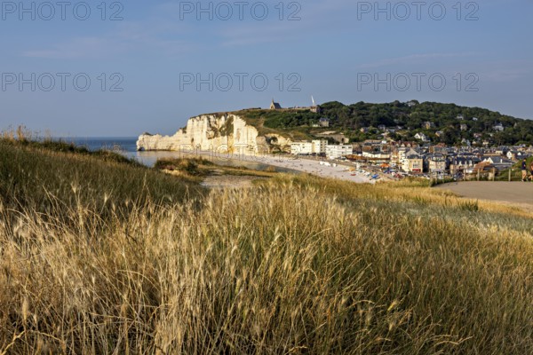 View of a seaside village with grassy cliffs overlooked by rocks, The cliffs and alabaster coast of Etretat in Normandy France