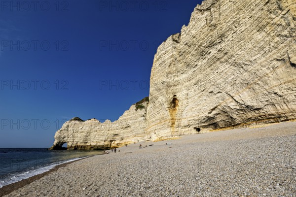 Large white rocks lining a pebble beach against the blue sky and sea, The cliffs and alabaster coast of Etretat in Normandy France