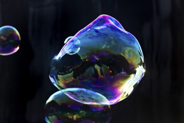 Large, irregular, iridescent soap bubbles in the colours of the rainbow against a black background, Recklinghausen, Germany