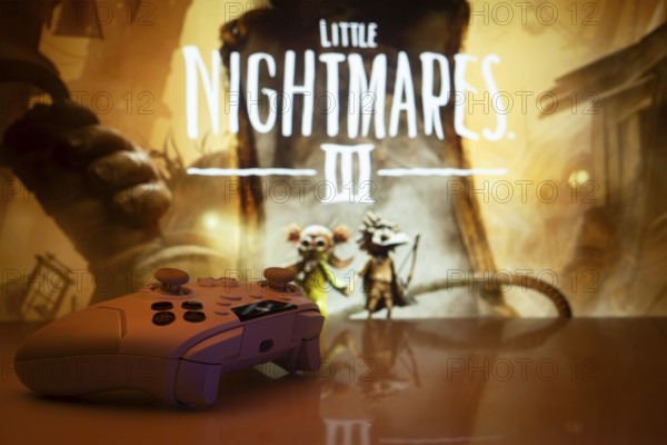Dhaka, Bangladesh- 22 July 2025: A close-up of a gamepad with the little nightmares 3 seen on screen in the background. Little Nightmares III is an upcoming horror adventure video game
