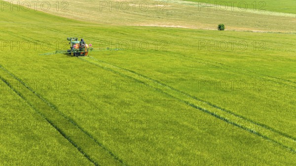 Farmer with tractor working in the field. In early summer, he fertilises the grain for an optimum yield. Drone photo. Merklingen, Baden-Württemberg, Germany
