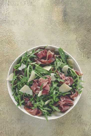 Fresh arugula salad with prosciutto and grated parmesan cheese, on a plate, homemade, no people