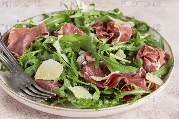 Fresh arugula salad with prosciutto and grated parmesan cheese, on a plate, homemade, no people