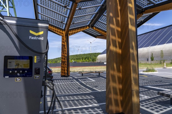 Electric charging station on the site of the former Lohberg colliery in Dinslaken, operated by Fastned, uses electricity from wind power and solar energy, fast-charging columns, with its own solar roof, in the background the 11, 500 square metre solar roof on the colliery's former coal mixing hall, wind farm on the Lohberg slagheap, North Rhine-Westphalia, Germany
