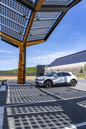 Electric charging station on the site of the former Lohberg colliery in Dinslaken, operated by Fastned, uses electricity from wind power and solar energy, fast-charging columns, with its own solar roof, in the background the 11, 500 square metre solar roof on the colliery's former coal mixing hall, wind farm on the Lohberg slagheap, North Rhine-Westphalia, Germany