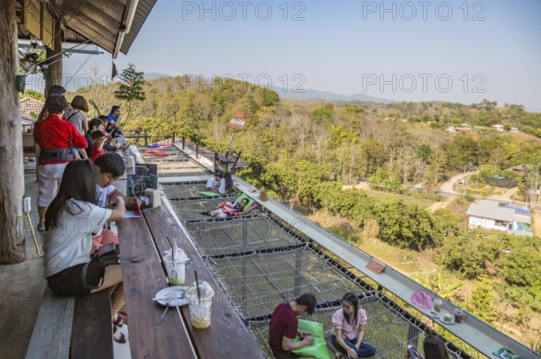 Customers eat, drink and relax on a net suspended over the hillside at the Akha Cottage restaurant and coffee shop in Chiang Rai, Thailand