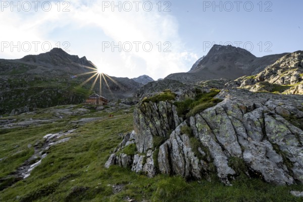 Mountain hut Elberfelderhütte in front of a rocky mountain landscape, sun star in the morning, in the upper Gössnitz valley, Wiener Höhenweg, Schober group, Hohe Tauern National Park, Carinthia, Austria