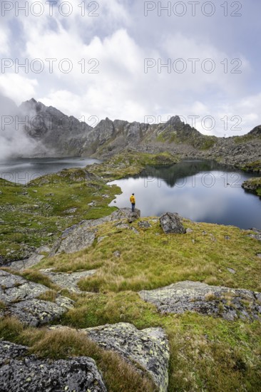 Mountaineer on a rock in front of mountain lakes Wangenitzsee and Kreuzsee, cloudy mountain peaks in the morning, Schober group, Hohe Tauern National Park, Carinthia, Austria