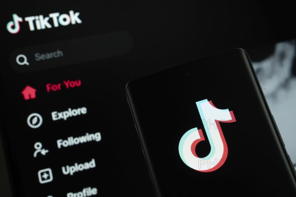 Dhaka, Bangladesh - 18 March 2025: The logo of the tiktok is displayed on a smartphone screen, and the website tiktok is visible on a computer screen in the background