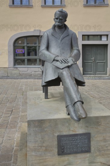 Monument to philosopher Friedrich Nietzsche, bronze sculpture, modern art, sitting on chair with book, inscription, Holzmarkt, Saale, Naumburg, Saxony-Anhalt, Germany